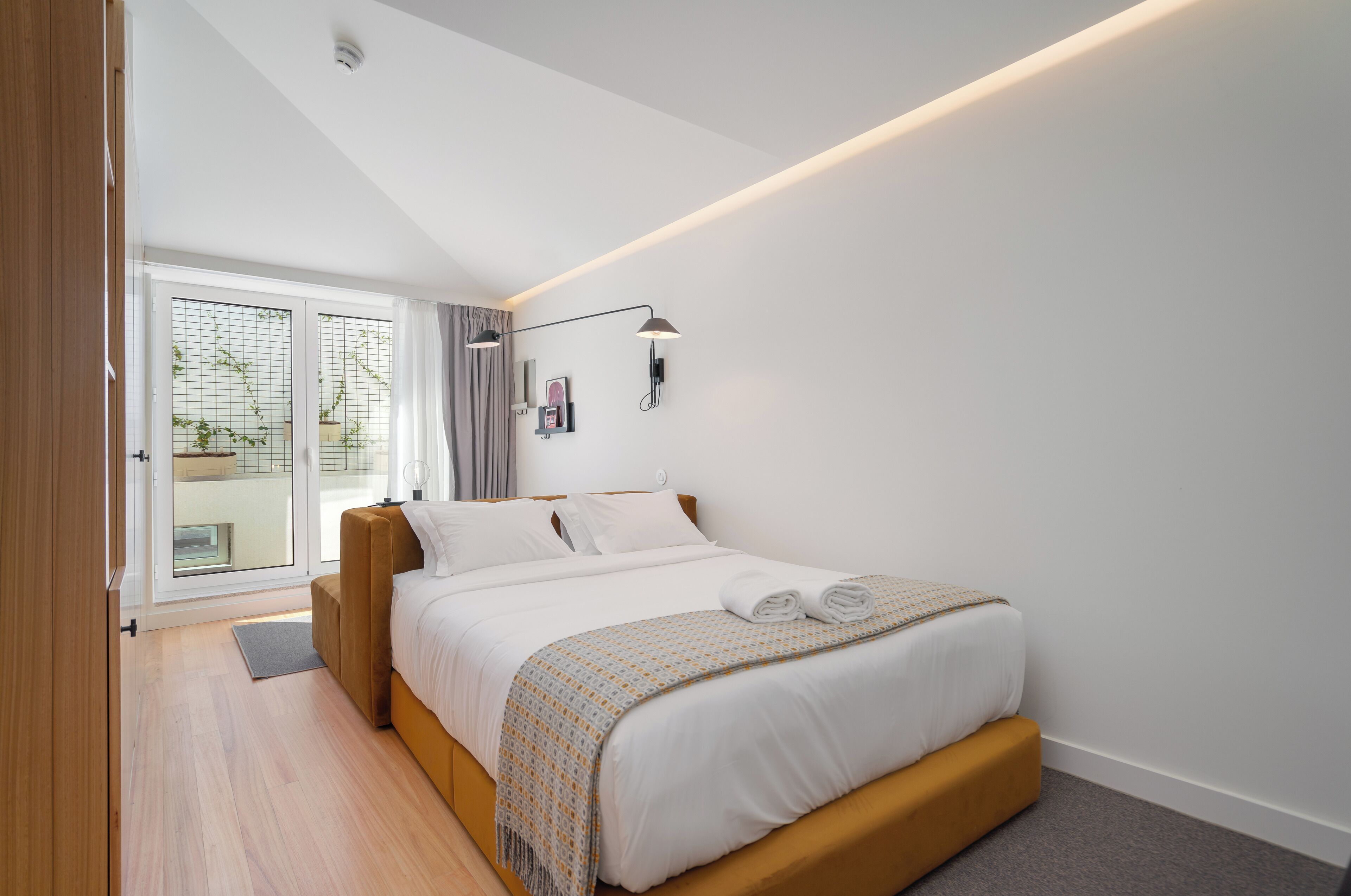 Ein modernes Schlafzimmer mit Bett, Nachttischen, einem Fenster mit Vorhängen und Blick ins Freie.