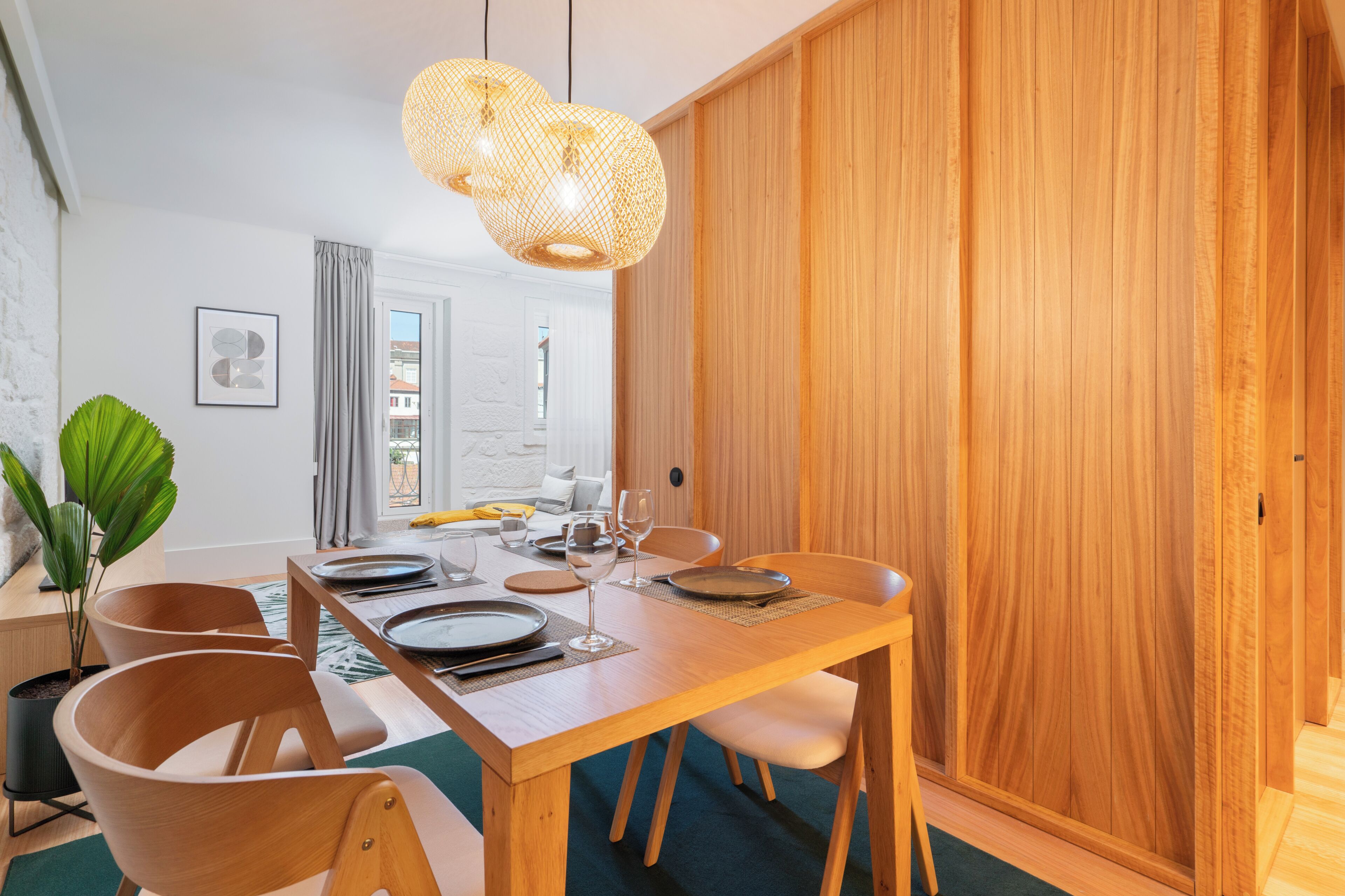 A dining area with a wooden table set for four, two pendant lights, and a potted plant.