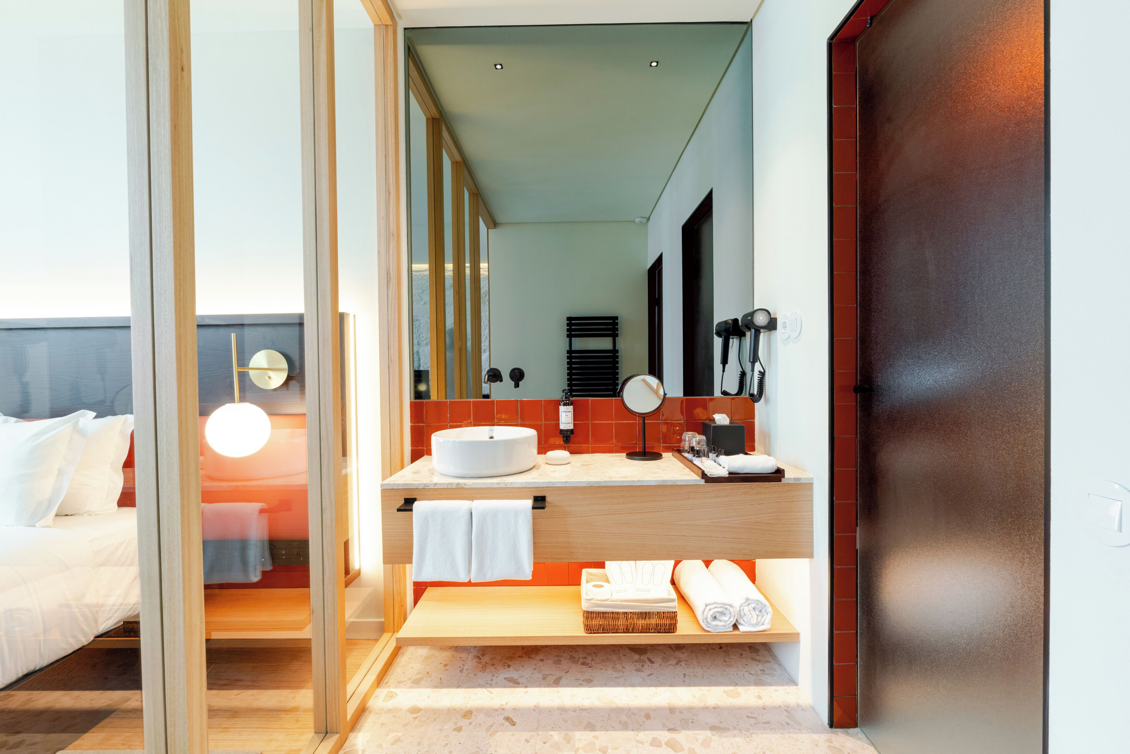 A modern hotel bathroom with a large mirror, a round sink, and a wooden vanity.