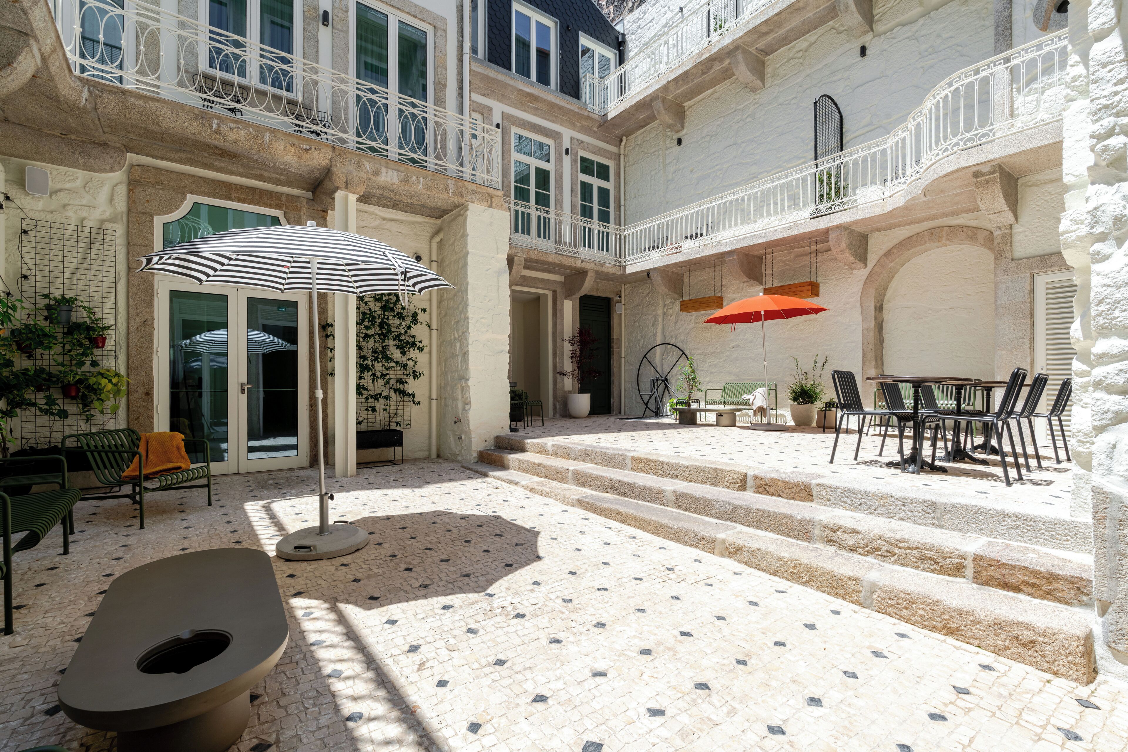 A courtyard with a stone floor, outdoor seating, and a staircase leading to an upper level.