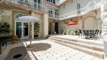 A courtyard with a stone floor, outdoor seating, and a staircase leading to an upper level.