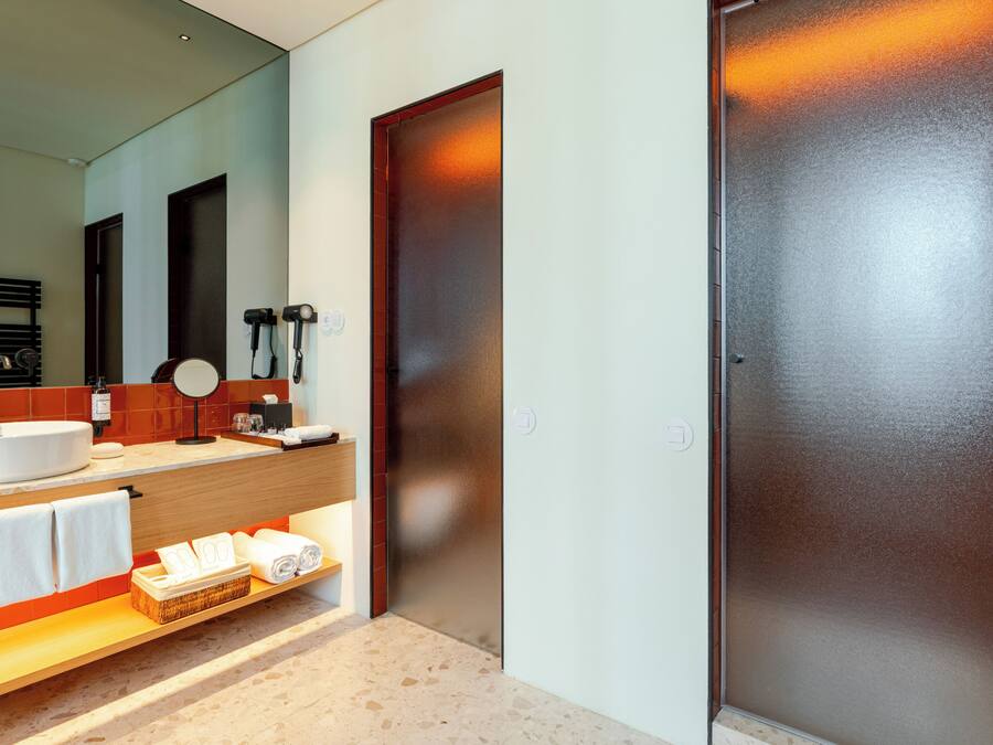 Un baño moderno con un espejo grande, un lavamanos, un mueble de tocador y un perchero para toallas.