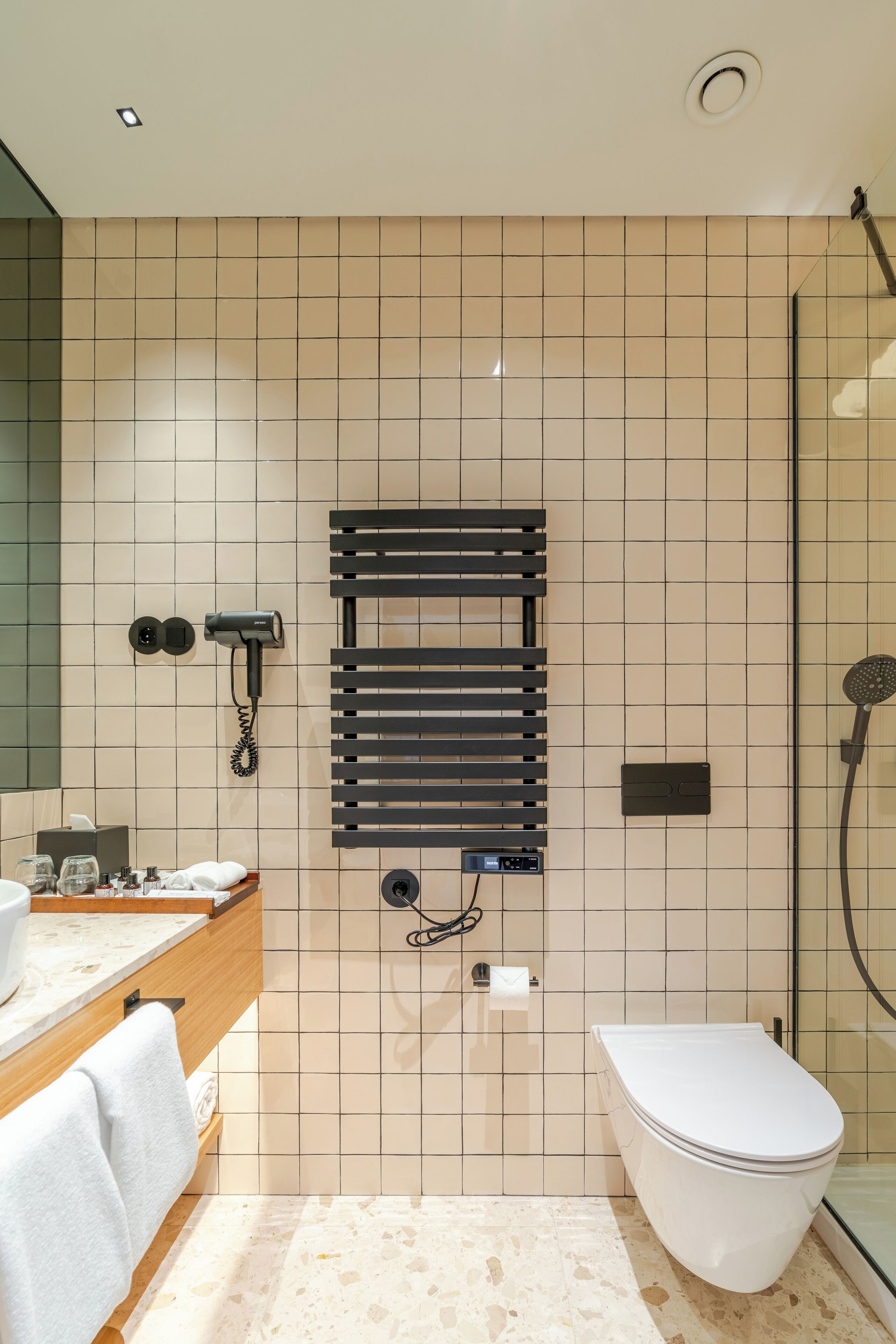 A modern bathroom with a glass shower enclosure, a built-in towel rack, a hairdryer, and a toilet.