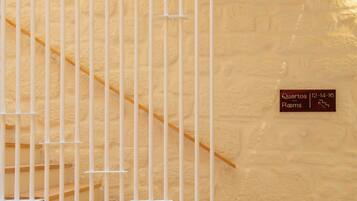 A staircase with white railings and a wooden handrail, leading to a landing with a sign indicating 'Quartos 12-14-16 Rooms'.