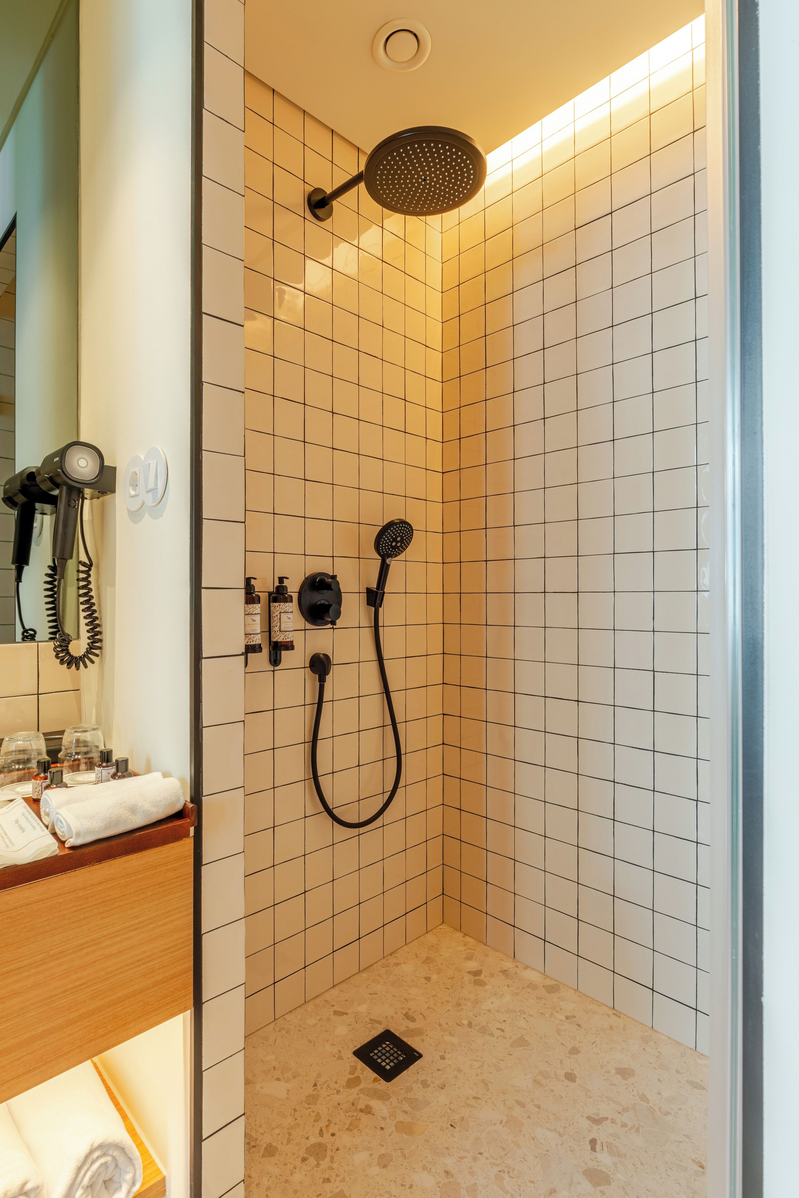 A small, tiled shower area with a handheld showerhead and a wall-mounted shower head.