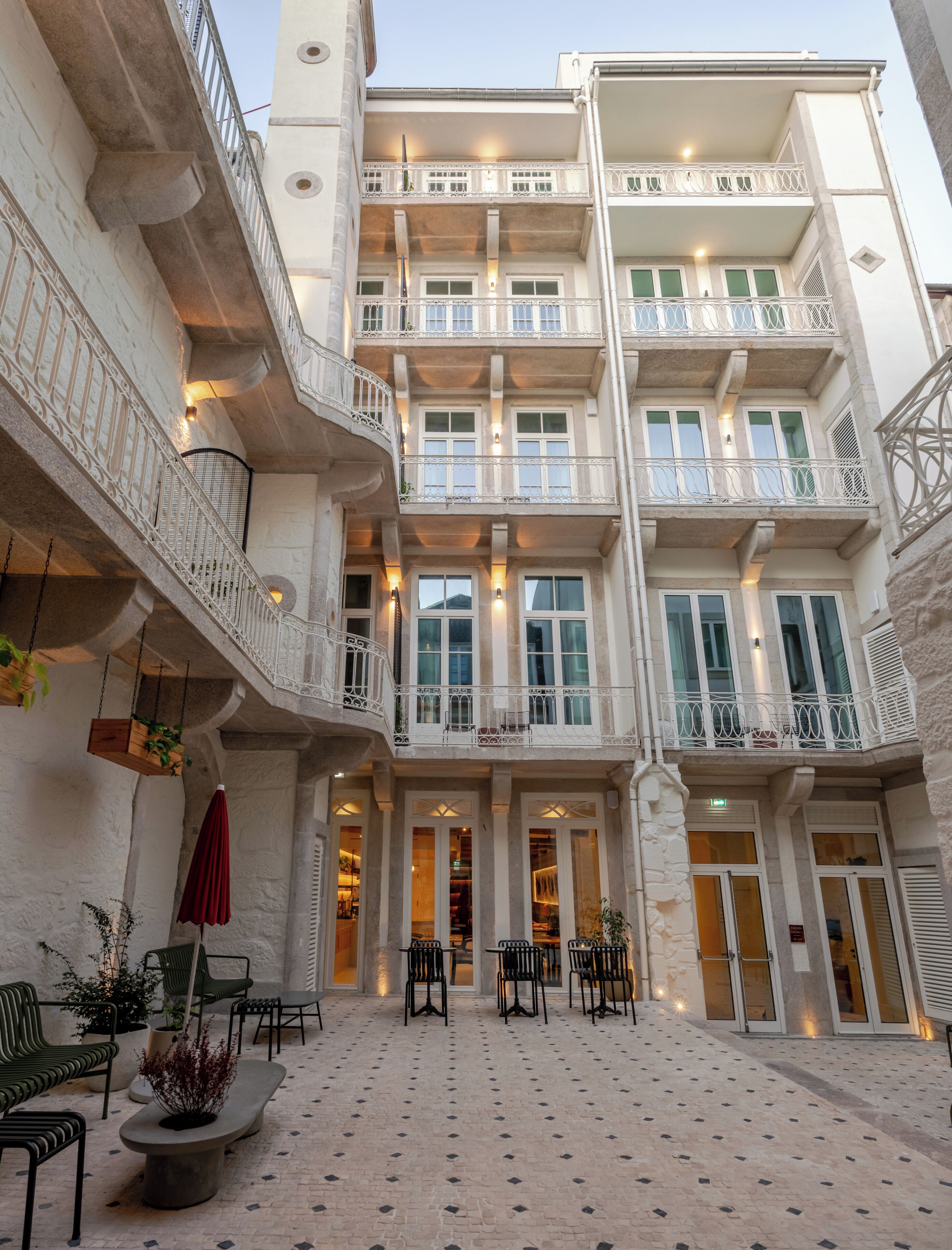 Un immeuble à plusieurs étages doté de balcons, d’un espace extérieur aménagé pour s’asseoir et d’une cour dallée.