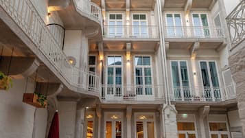 Un immeuble à plusieurs étages doté de balcons, d’un espace extérieur aménagé pour s’asseoir et d’une cour dallée.
