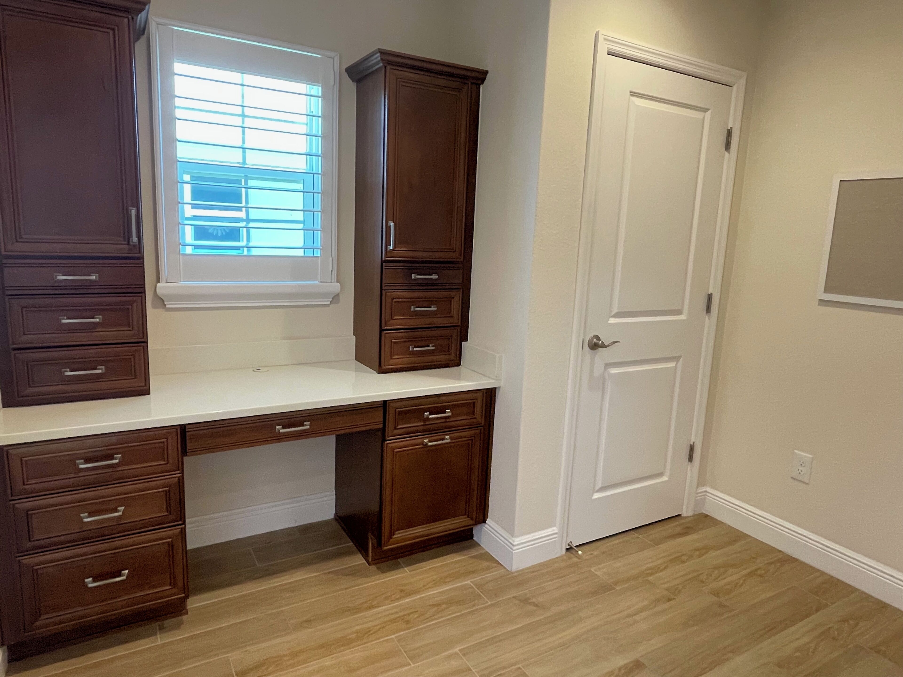 A room with a desk, drawers, a window, and a door.