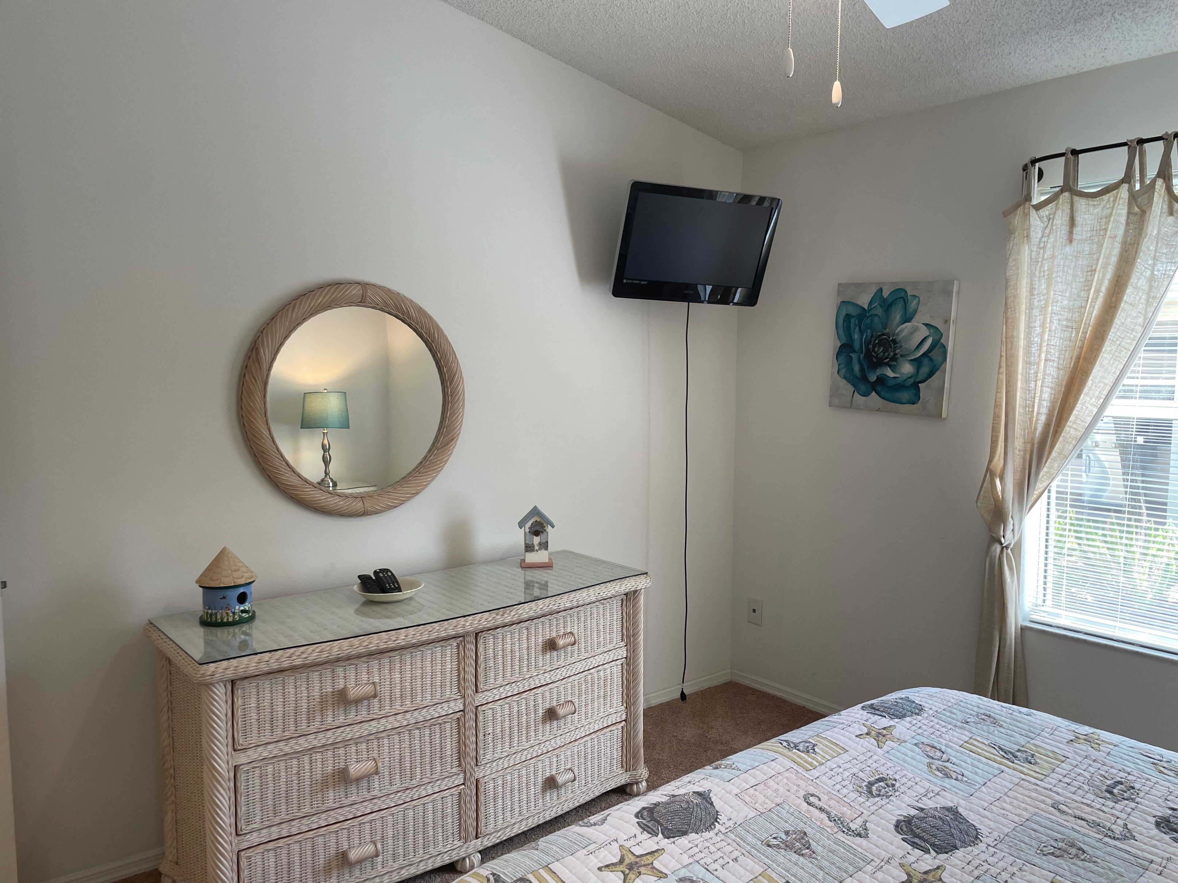 Une chambre à coucher avec un lit, une commode, une télévision et une fenêtre avec des rideaux.