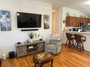 Ein Wohnzimmer mit Flachbildfernseher, einer Couch, einem Couchtisch und einer Küchenzeile mit Holdekor und einer Mikrowelle.
