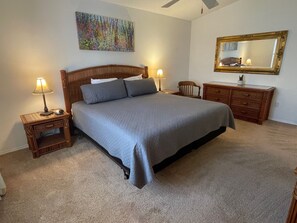 Ein Schlafzimmer mit einem Bett, zwei Nachttischen mit Lampen, einem Schminktisch, einem Sessel, einem Spiegel und einem Bild an der Wand.