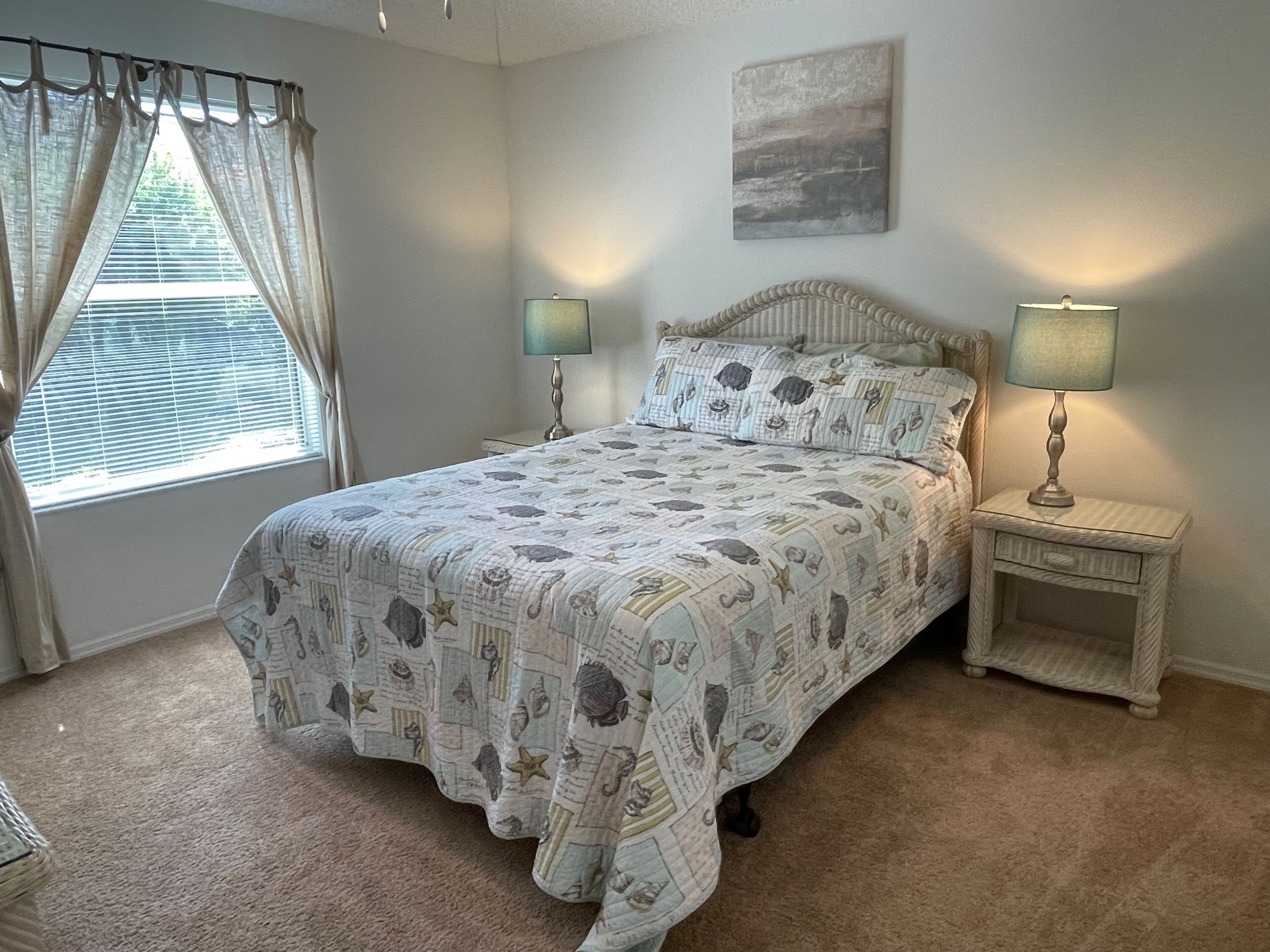 Une chambre à coucher avec un lit, deux tables de chevet avec des lampes, une fenêtre avec des rideaux et un tableau accroché au mur.
