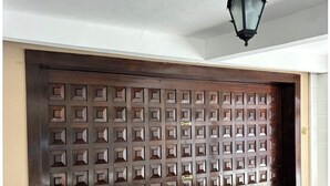 A closed wooden door with a geometric pattern, a hanging lantern, and a paved floor with yellow markings. - Entire Mansion 278 in Morumbi | Luxury, Comfort and Privacy (Morumbi)