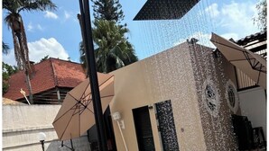 A swimming pool with a pink flamingo float, a water fountain, and a building with a tiled roof in the background. - Entire Mansion 278 in Morumbi | Luxury, Comfort and Privacy (Morumbi)