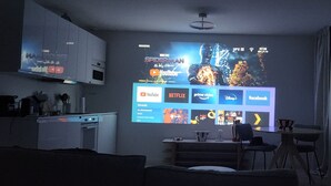 Ein Wohnzimmer mit an der Wand befestigtem Fernseher, der verschiedene Streaming-Dienste anzeigt.