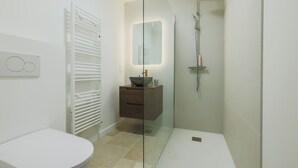 Ein modernes Badezimmer mit Toilette, einer gläsernen Dusche, einem Waschtisch mit Spiegel und einem Handtuchhalter.