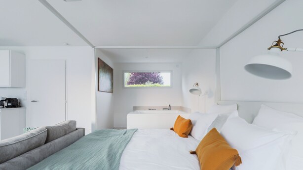 Ein modernes Schlafzimmer mit einem Bett, einem Schreibtisch und Blick auf Bäume.