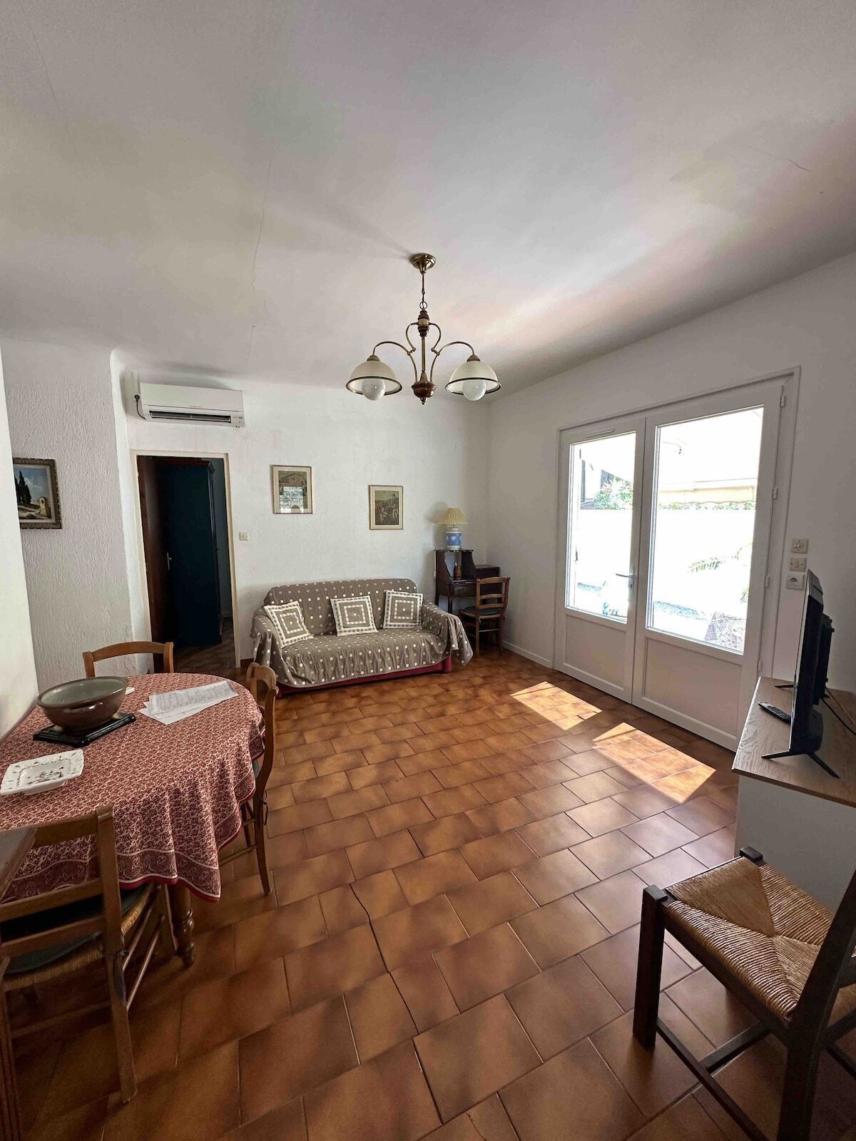 Un salon comprenant un canapé, une table à manger, des chaises, un téléviseur et une grande fenêtre.