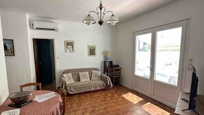 Ein Wohnzimmer mit einer Couch, einem Esstisch, Stühlen, einem Fernseher und einem großen Fenster.