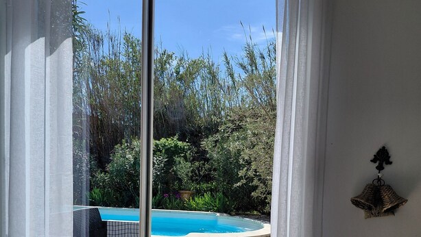 Quarto com porta de vidro deslizante que dá para área externa com piscina e vegetação.