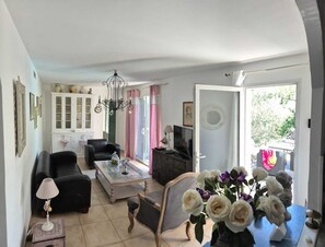 A living room with a sofa, a coffee table, a TV, and a chandelier. - 135m2 villa in Provence  (Cheval-Blanc)