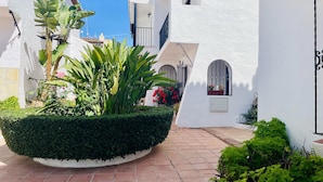 A courtyard with white walls, a tiled floor, and a large planter with various plants. - Azure Apartment Burriana by At Home Costa del Sol (Nerja)