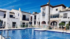 A swimming pool with a clear blue water surface, surrounded by white buildings with balconies and satellite dishes. - Azure Apartment Burriana by At Home Costa del Sol (Nerja)