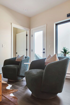 Ein modernes Wohnzimmer mit zwei grünen Sesseln, einem kleinen weißen Tisch und einem großen Fenster mit Blick.