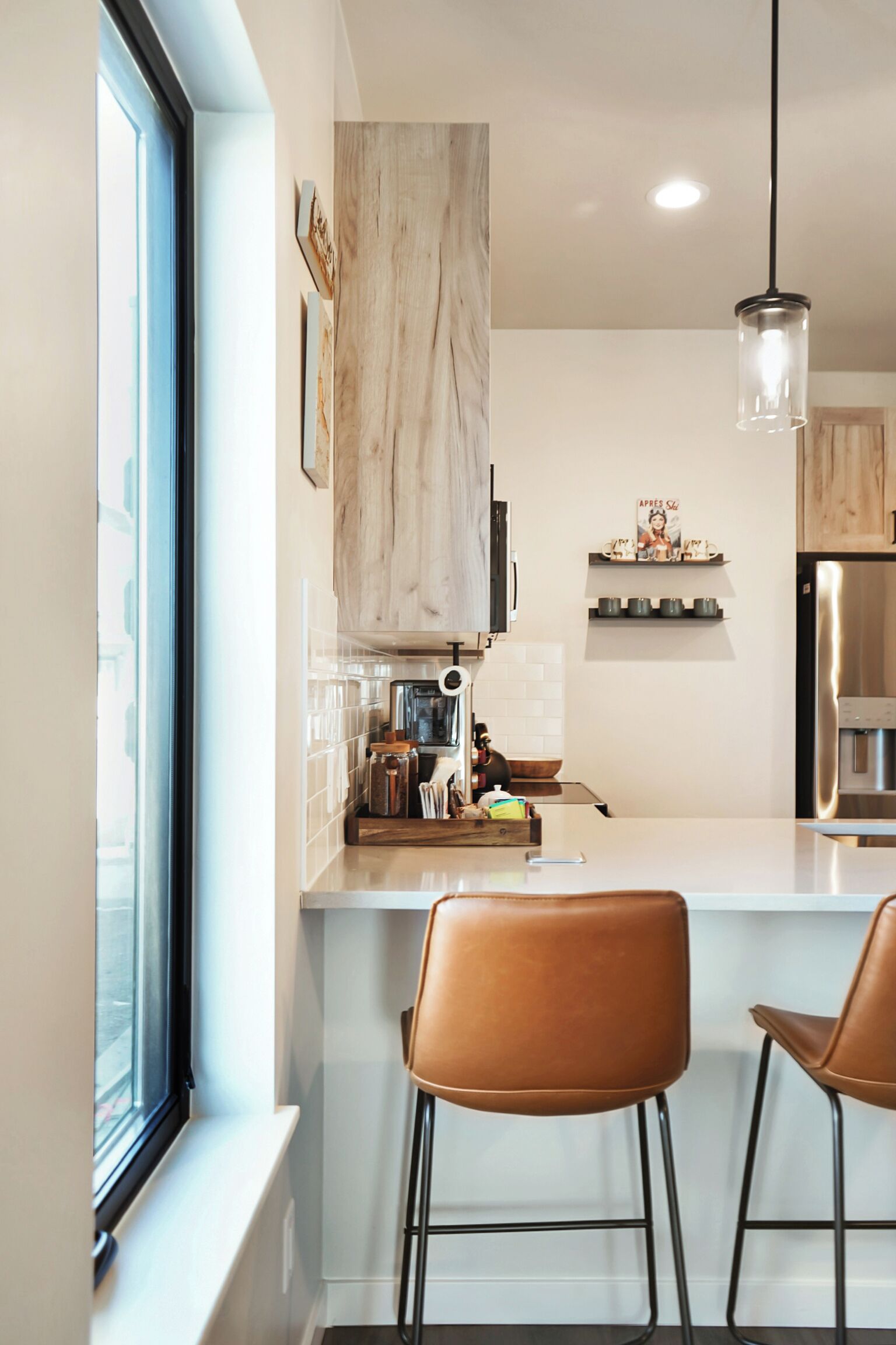 Een moderne keuken met een groot raam, een hanglamp en twee barkrukken.