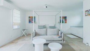 Uma sala de estar moderna e minimalista com um sofá cinzento, duas mesinhas de apoio brancas, um projetor de teto branco e arte abstrata nas paredes.