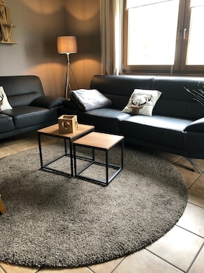 Un salon avec un canapé en cuir noir, un tapis rond de couleur grise, une table basse en bois et un lampadaire.
