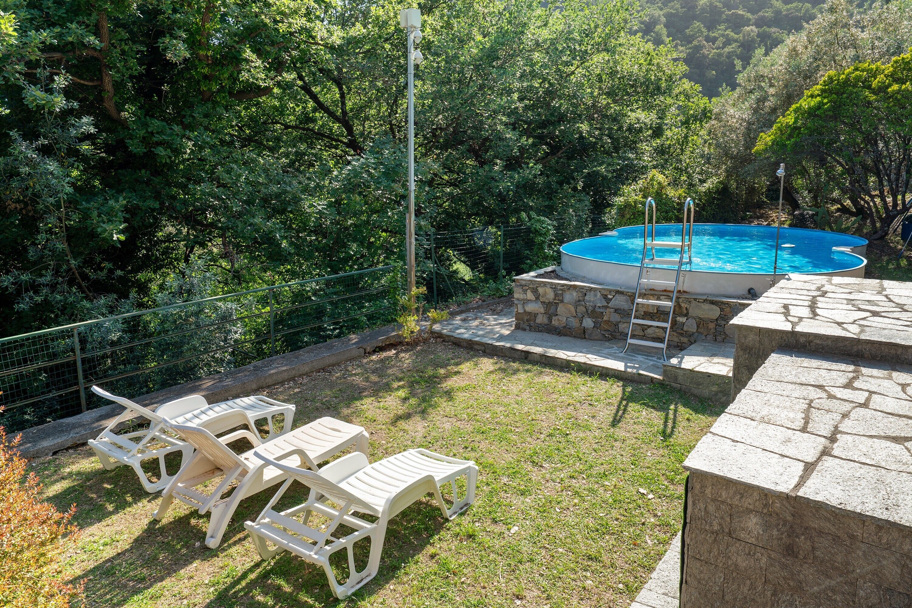 A backyard with a swimming pool, a stone deck, and white plastic lounge chairs.