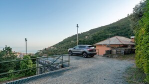 A gravel driveway leading to a building with a tiled roof, surrounded by greenery and overlooking a hilly landscape.