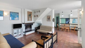 A living room with a fireplace, sofa, TV, and dining area with chairs.
