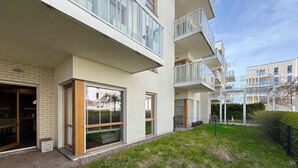 Un moderno edificio residenziale con balconi, ampie finestre e un cortile lastricato d'erba.