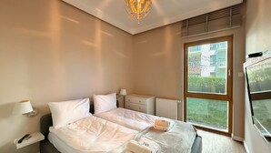 Una moderna camera d'albergo con un letto grande, comodini, una lampada, un termosifone e una finestra con vista sul verde.