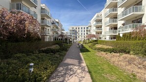 Un sentiero costeggiato da moderni palazzi con balconi, cielo sereno e vegetazione.