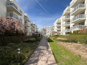 A pathway flanked by modern apartment buildings with balconies, a clear sky, and greenery. - Mila Baltica Q4 Apartments (Gdańsk)