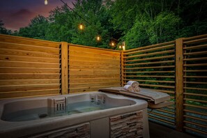 A wooden spa area with a hot tub, stone accents, and string lights.