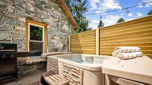 Eine Fassade aus Stein, eine Holzterrasse, ein Whirlpool und ein Grill.
