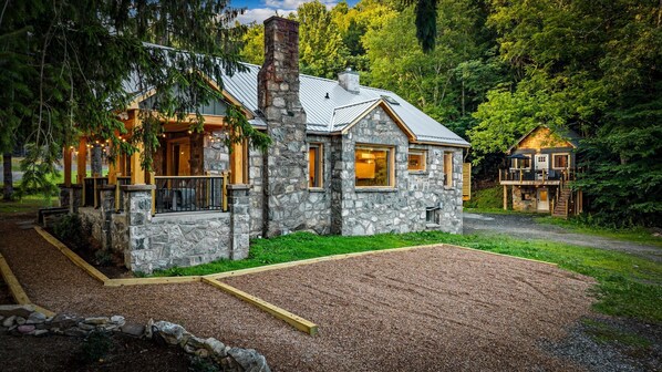 A stone house with a chimney, large windows, and a deck.