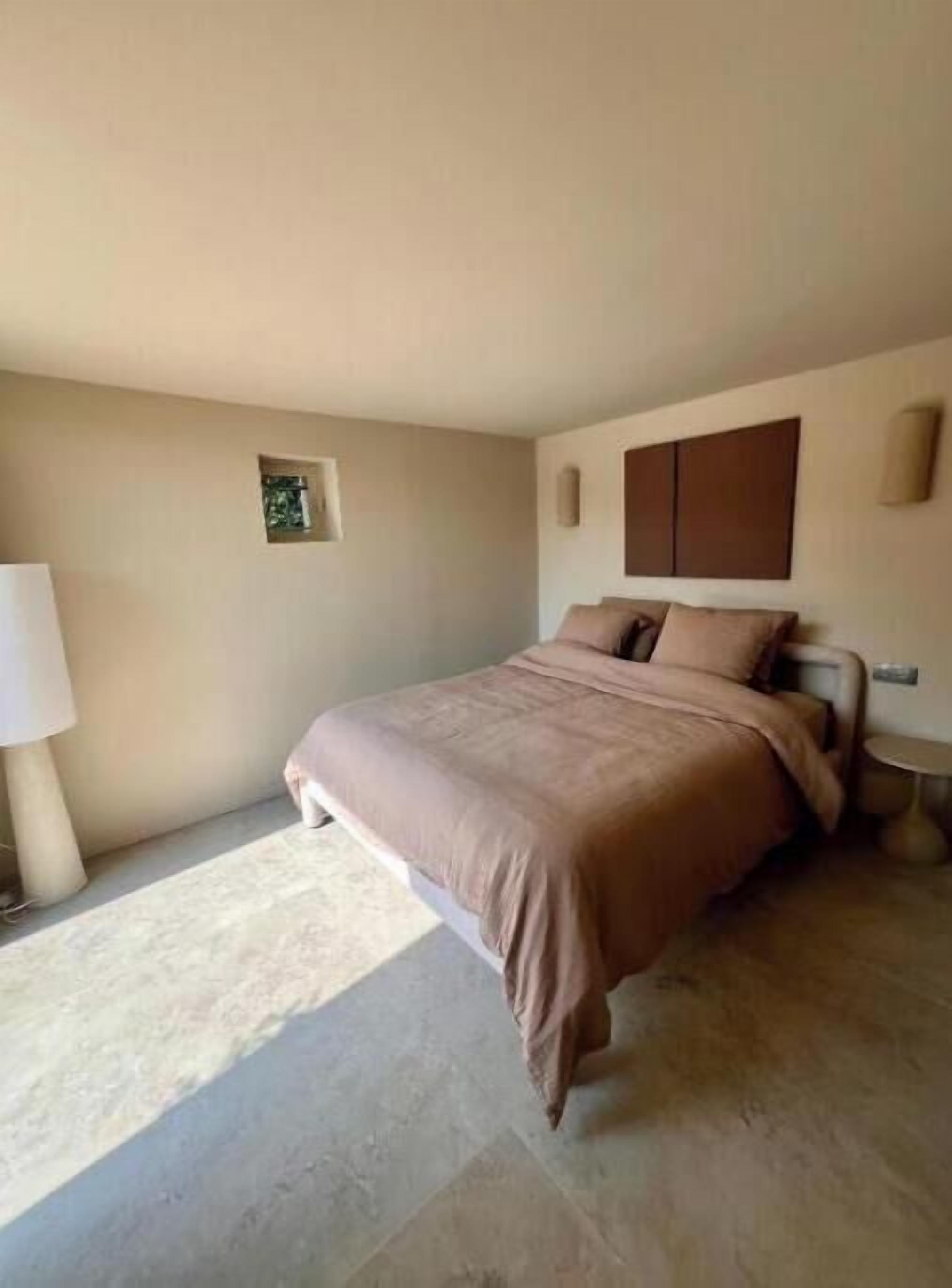 A bedroom with a bed, a nightstand, a lamp, and a small picture frame on the wall.