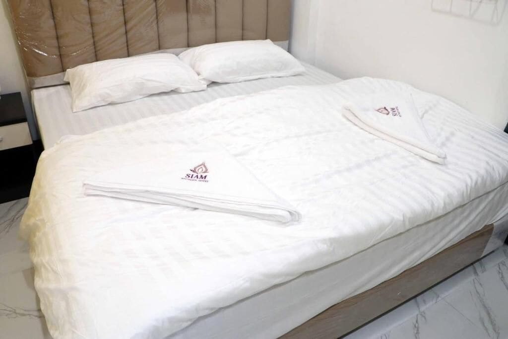 A bed with white bedding and pillows, a wooden headboard, and a logo on the bedspread.