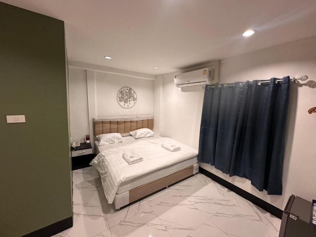 A bedroom with a bed, a nightstand, an air conditioning unit, and a shower curtain.