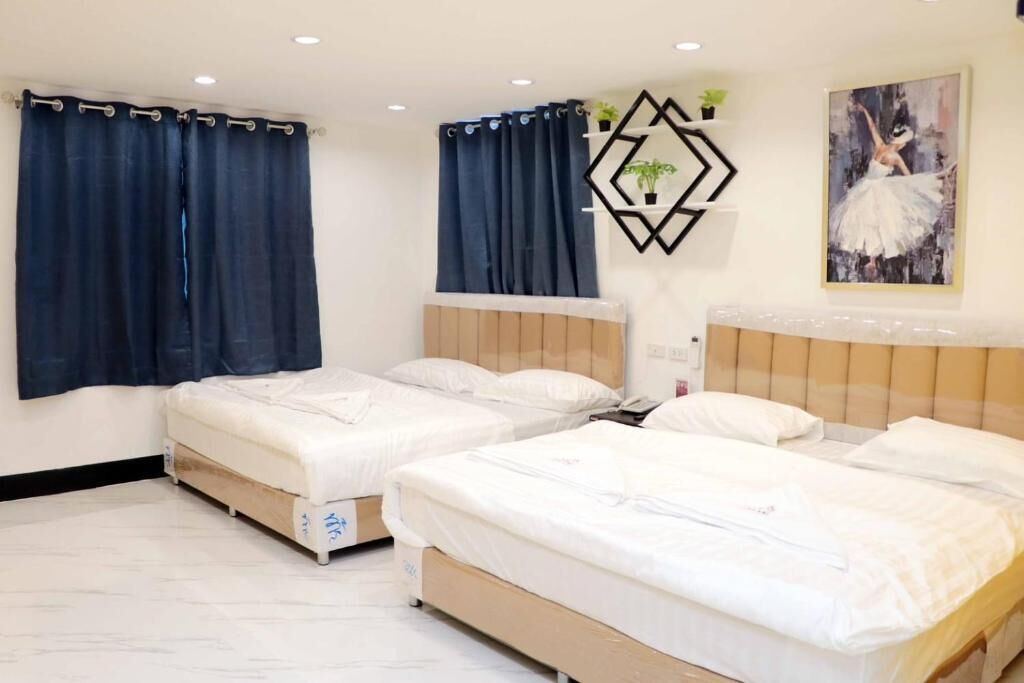 A hotel room with two single beds, dark curtains, a wall-mounted geometric decoration, and a ballet dancer painting.