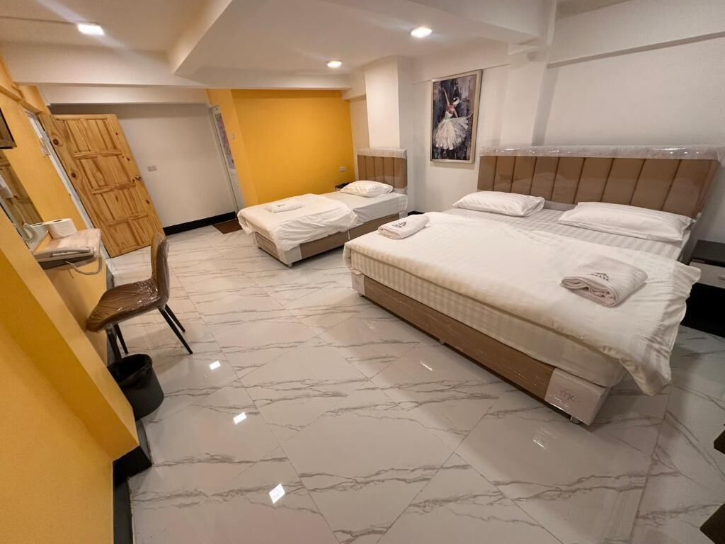 A hotel room with three beds, a wooden wardrobe, a mirror, and a marble floor.
