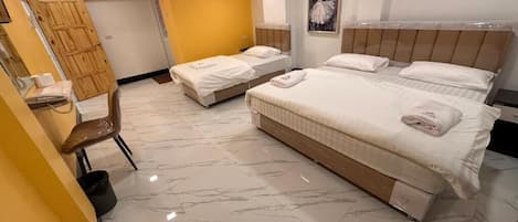 A hotel room with three beds, a wooden wardrobe, a mirror, and a marble floor.