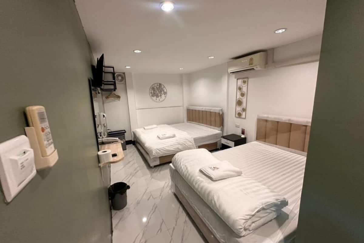 Habitación de hotel con dos camas, una mesita de noche pequeña, aire acondicionado en la pared, un espejo y un cubo de basura.