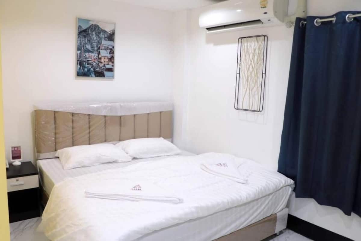 Habitación de hotel con cama, mesita de noche, aire acondicionado, cortina y una obra de arte colgada en la pared.