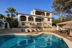 Ein zweistöckiges Haus mit Swimmingpool, Sitzgelegenheit im Freien und einer Steinmauer.